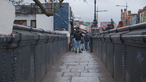 People-Walking-Across-Bridge-Over-Camden-Lock-In-North-London-UK
